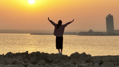 Aerial View of a Happy Woman Raising Her Hands Up at Sunset on the Seashore