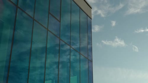 Cloud reflections on a blue glass building against a clear sky.