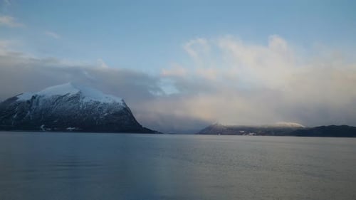 Scenic fjord with clouds above the mountains and the landscape is covered with snow on a bright