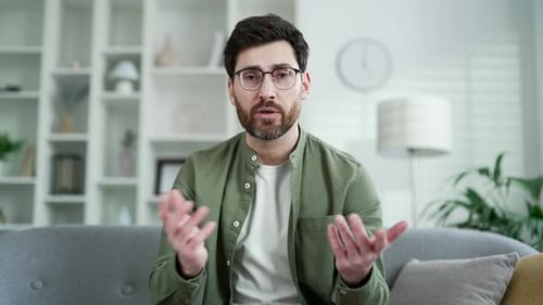 Webcam view. Businessman talking on a video call looking at camera sitting on sofa in living room