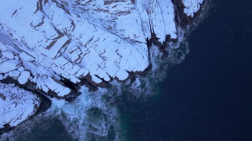Snowy cliffs and icy waters meet the ocean in Lofoten, Norway, with a stunning lighthouse pan