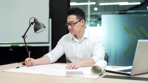 Asian creative designer or architect working in the office at work at a computer desk with drawings.
