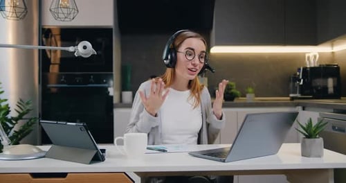 Una joven caucásica positiva con auriculares se comunica a través de las conversaciones del operador del centro de videollamadas