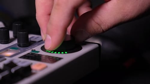 Human finger adjusting audio mixer knob for volume control in recording studio.