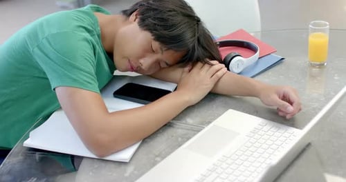 Teenage Asian boy rests his head on a desk while studying, with copy space