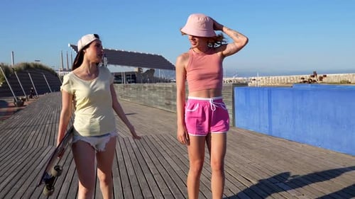 Two young women walking and talking on a boardwalk