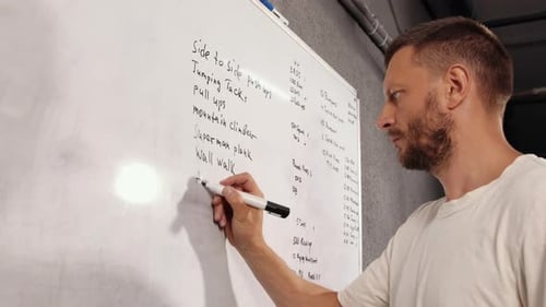 Athlete in White t Shirt Writes Down Exercises That He Will Perform on White Board with a Marker