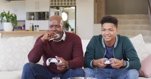 Excited african american father and adult son playing video game and celebrating, slow motion