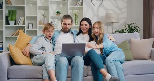 Happy family sitting together on couch in living room having fun on internet using laptop