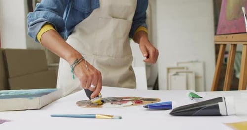 Artist mixes paint on a palette in a bright studio, with copy space