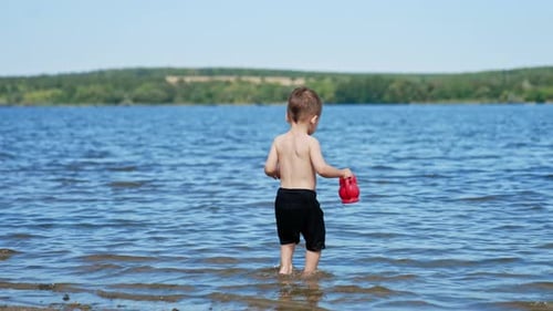 Summer sunny day and splashing on a beach. Small funny child playing on river with water.
