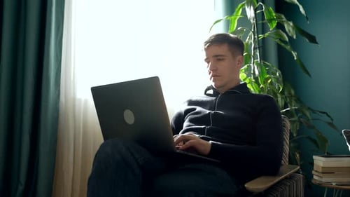 Man Sitting in Chair Using Laptop at Home