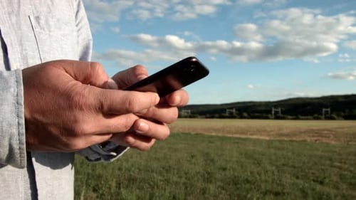 View of a hand holding a cell phone in the middle of nature