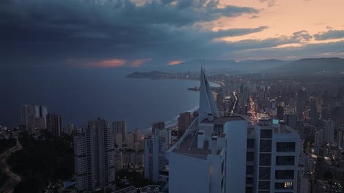 Seafront modern city next to the deep blue ocean at night. Orange sunset and dark stormy clouds.