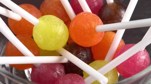 Colorful lollipops or candy bonbons on a stick rotate in glass bowl side view. Holiday sweet