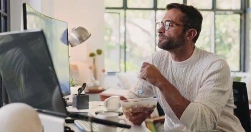 Man, eating and reading report at desk in office with salad, multiscreen setup and working lunch