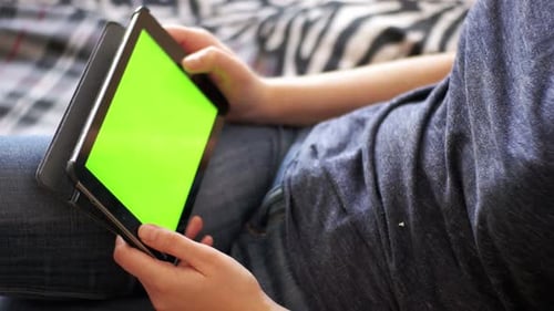 Young Woman Lying on Bed and Using Tablet with Green Screen at Home