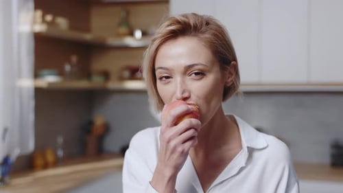 Woman Eating an Apple in Her Kitchen