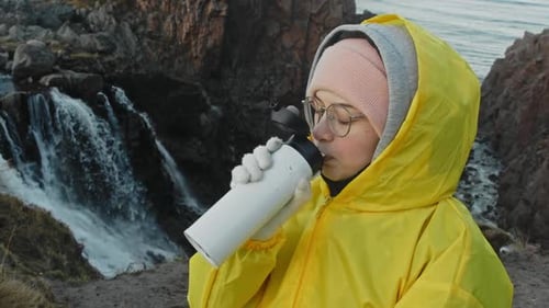 Young Adult Drinks Water by Scenic Waterfall