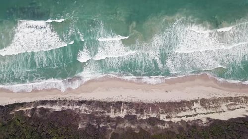 Aerial View of Turquoise Waves Crashing on a Sandy Beach Surrounded By Lush Greenery in a Tranquil