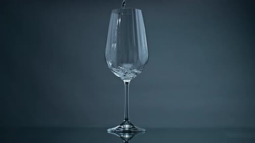 Wassergießendes Weinglas mit dunklem Hintergrund in Nahaufnahme. Klare Flüssigkeit spritzt hinein