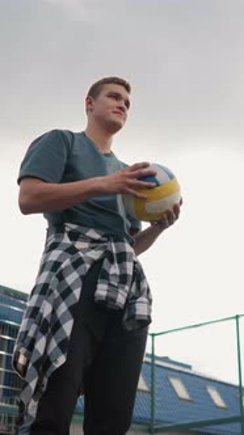 Young Man Rotating Volleyball in Hand with Plaid Shirt and Outdoor Court Background