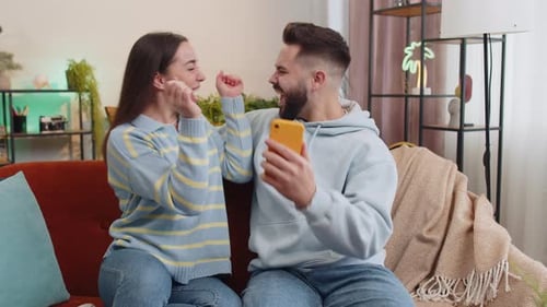 Couple Celebrating Success Together on Smartphone Indoors