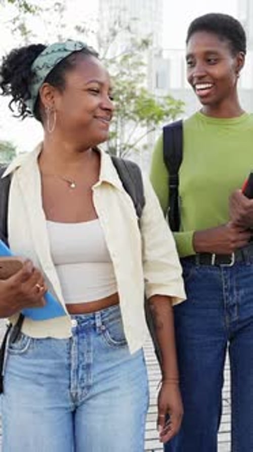 Estudiantes universitarias afroamericanas charlando mientras caminaban fuera del campus después de los exámenes finales
