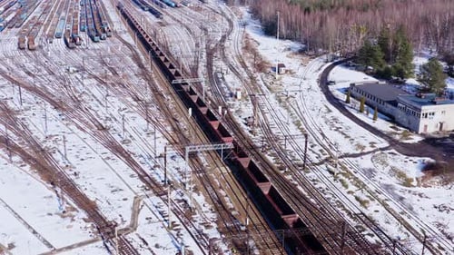 Aerial drone shot following a long empty freight train through the snow covered winter landscapes of