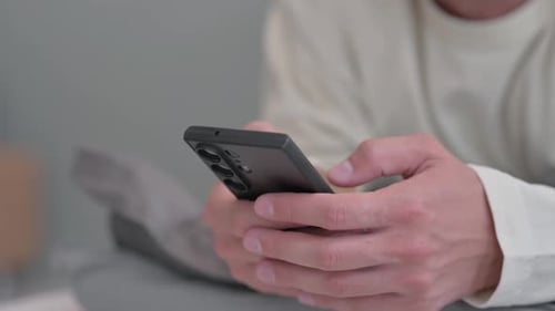 Close up of Male Hand Using Phone while Lying on Stomach in Bed
