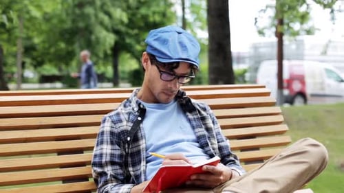 Young Man Sits on Bench Writing in Notebook