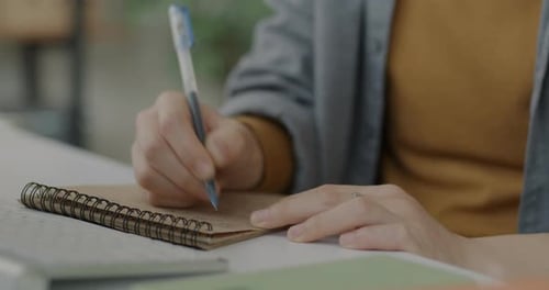 Closeup of Male Hand Writing in Notebook with Pen While Businessman Working at Office Desk