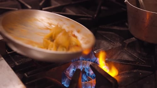 Pasta is shaken in a silver pan on the gas stove in a restaurant kitchen. Close up panning shot