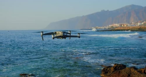 Drone Hovering Over Ocean Water Near Rocky Coastline
