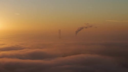 Factory Emitting Smoke Above The Clouds at Sunrise