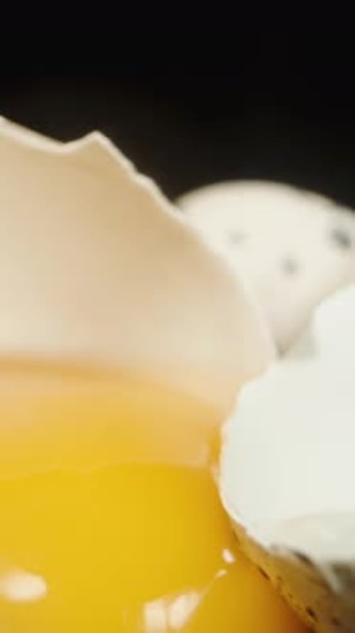 Vertical video. Quail eggs on a black table and background, one of them is cracked. Dolly