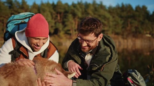 Couple of Two Smiling Gay Men Relaxing and Playing with Husky Near Lake in Spring