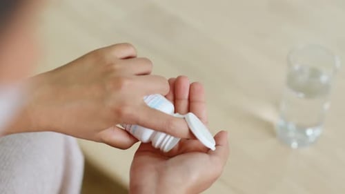 Woman Pours Green Pills into Hand Indoors