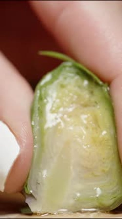 Vertical video. A female hand with white manicure squeezes a Brussels sprout, and juice slowly drips