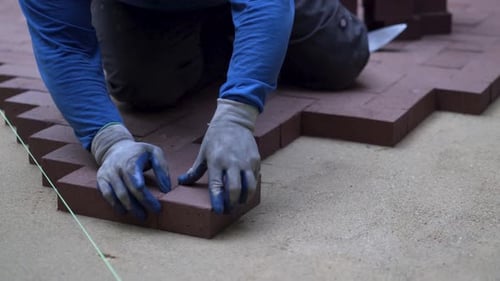 Man putting red brick pavers into place in a herringbone pattern on a bed of sand.