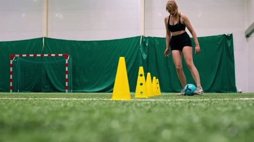 young girl is training on the soccer field driving the ball between the chips or cones preparing
