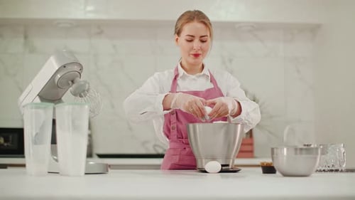 . A woman adds eggs to the metal bowl of a food processor to prepare the cheese base