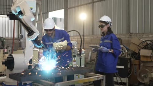 Blue collar workers at machine shop with welding robot arm.