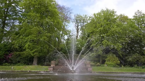A running fountain in the middle of calm water pond under a blue cloudy sky during the early sprint