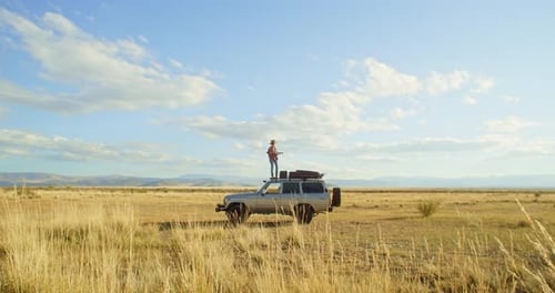 Woman Stands on Car During Grassy Plain Roadtrip