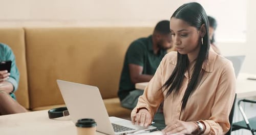 Focused creative businesswoman typing on laptop and writing notes in a notebook in office