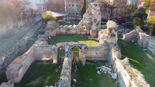 Drone flying backward and upward over old ruins of Roman Thermae in Europe with green grass reveal s