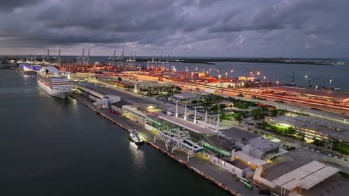 Industrial and public port of Miami with cranes and container at dusk. Lighting city of Miami with d