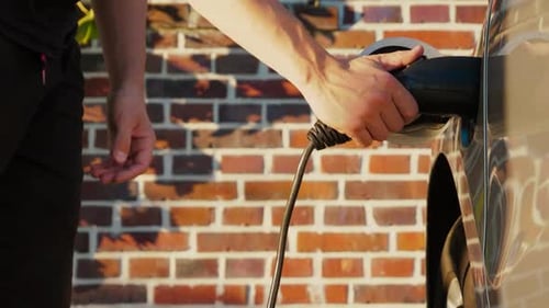Man Unplugs Charging Cable from Electric Vehicle