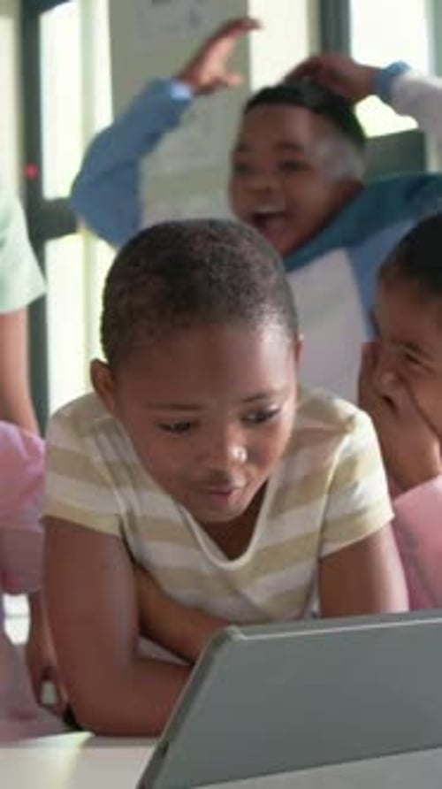 Vertical video: Pointing teacher aiding child in stripes tapping tablet in class, peers reacting